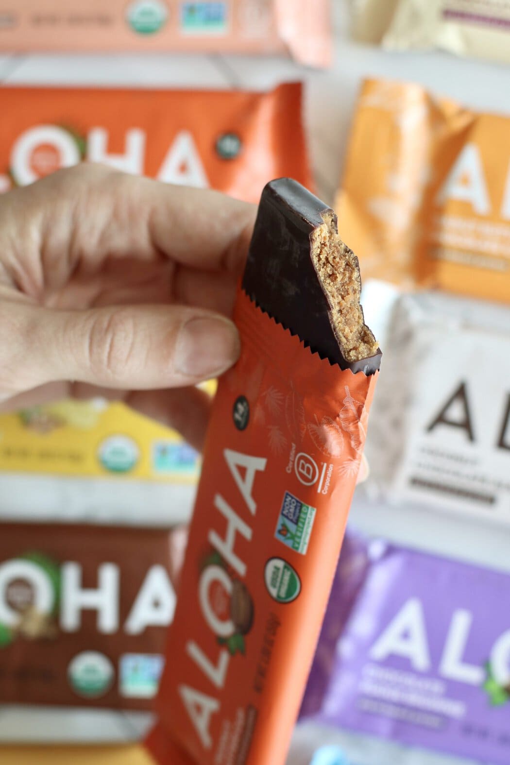 Close up view of a hand holding an aloha bar with a bite out of it to show the inside chewy texture.
