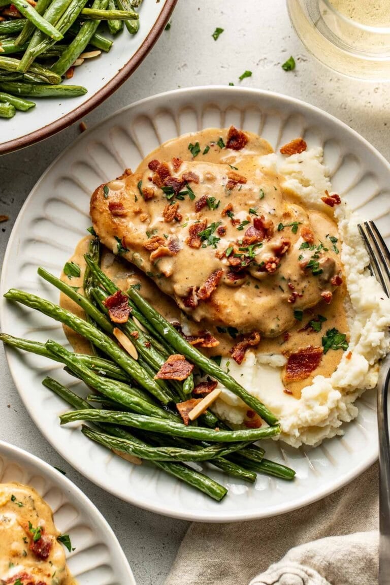 Overhead view of a plate filled with smothered chicken on top of mashed potatoes next to roasted green beans.