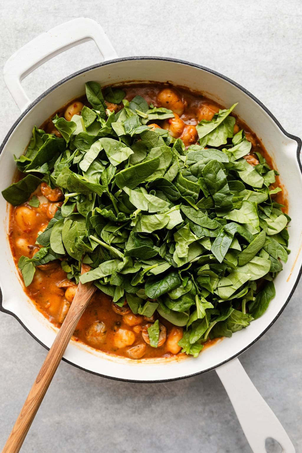 Overhead view of a skillet filled with Sausage And Gnocchi and topped with chopped spinach