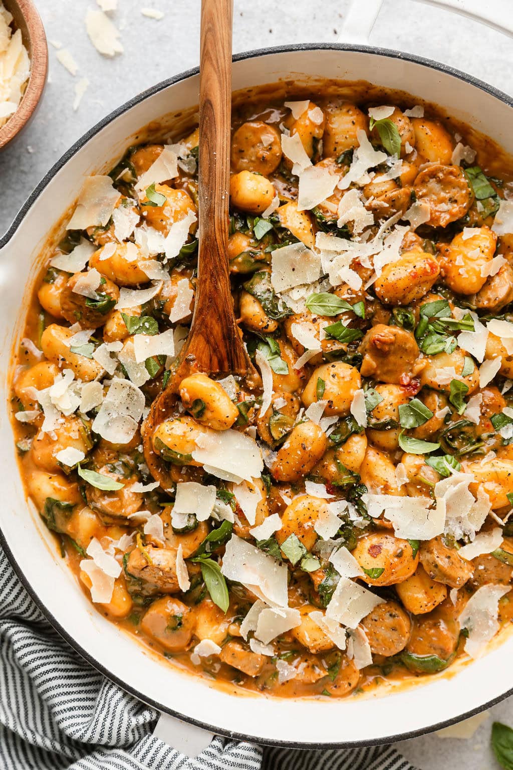 Overhead view of a skillet filled with Sausage And Gnocchi topped with fresh basil and shaved parmesan.