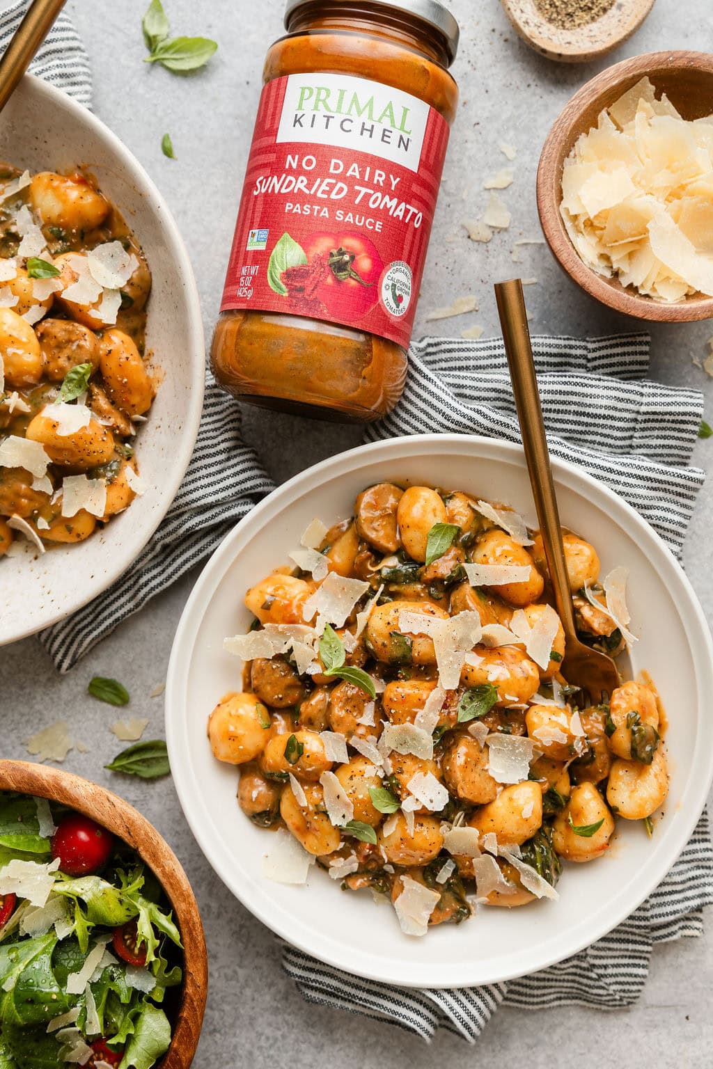 Overhead view of 2 bowls of Sausage And Gnocchi Skillet next to a jar of sundried tomato sauce