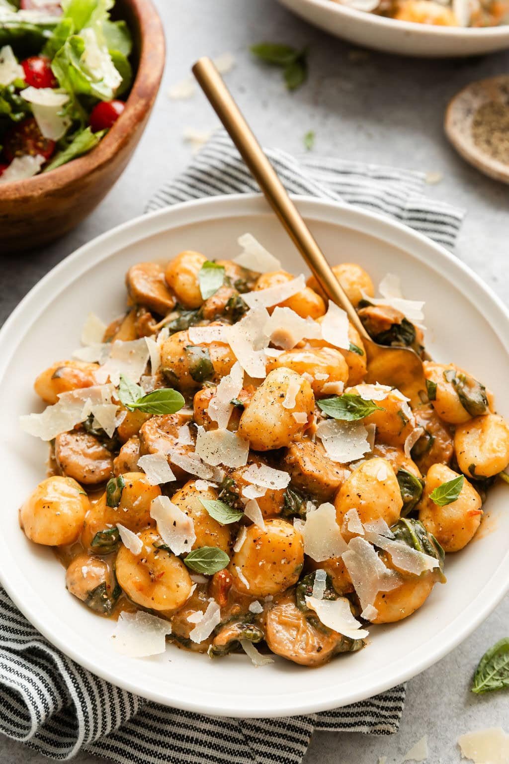 Close up view of a white bowl of Sausage And Gnocchi Skillet topped with fresh basil and shaved parmesan