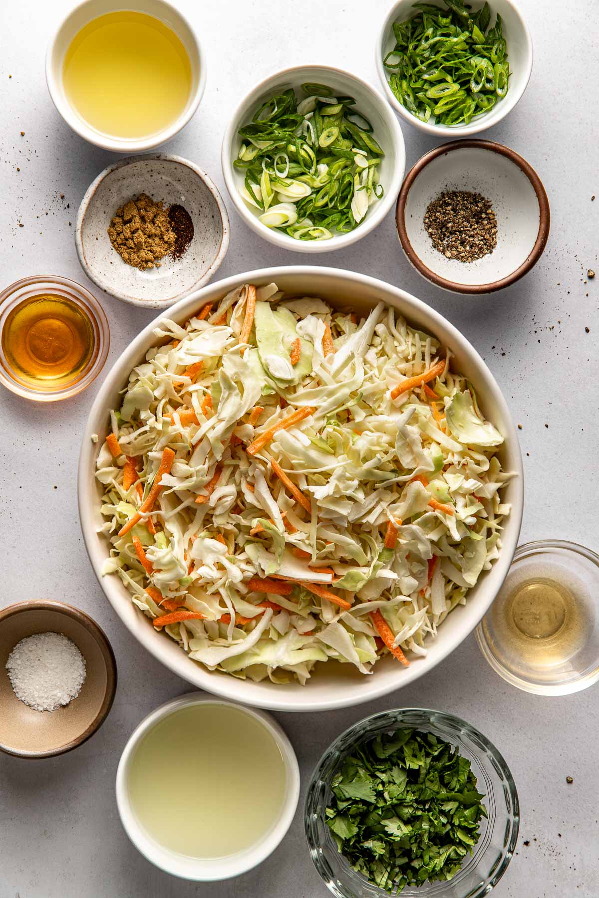 Overhead view of a variety of ingredients for Cilantro Lime Slaw in different sized bowls. 