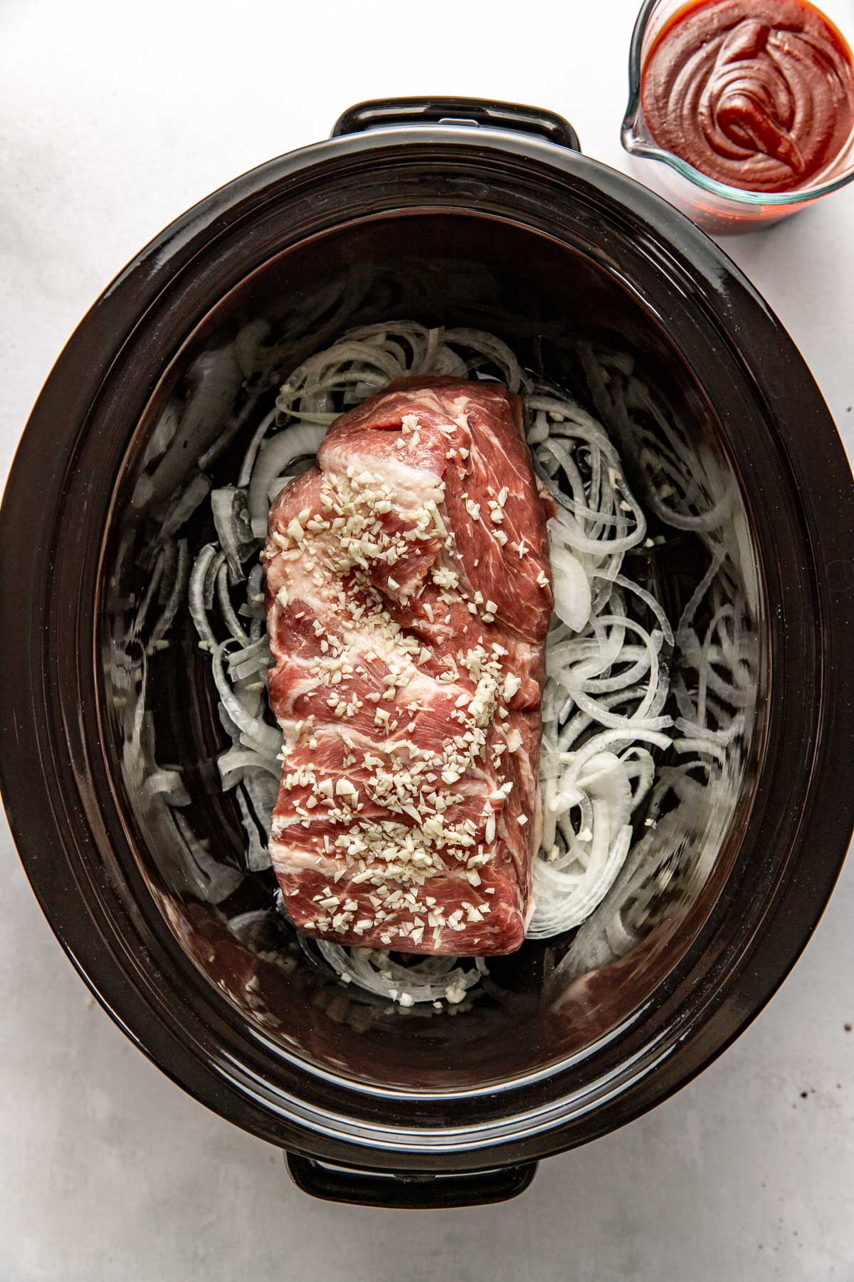 Overhead view of a pork roast and onions in a slow cooker. 
