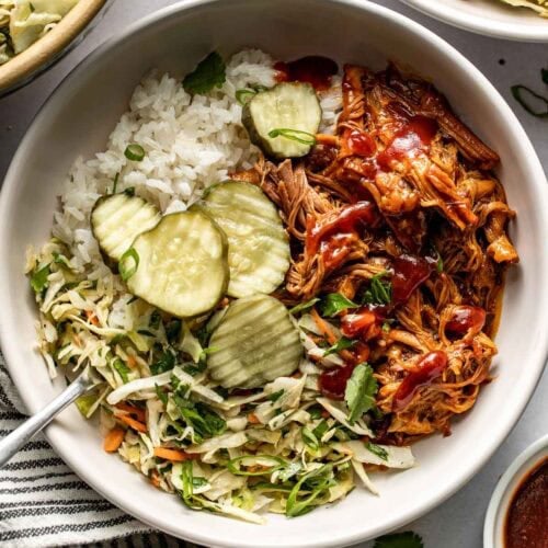 Overhead view pulled pork served over rice with slaw and pickles on the side.