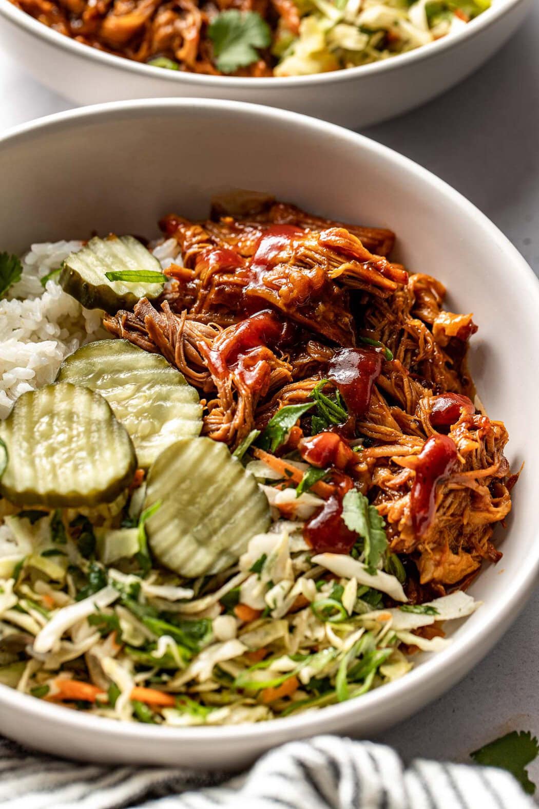 Close up view of a Pulled Pork Bowl topped with sliced dill pickles and green onions. 