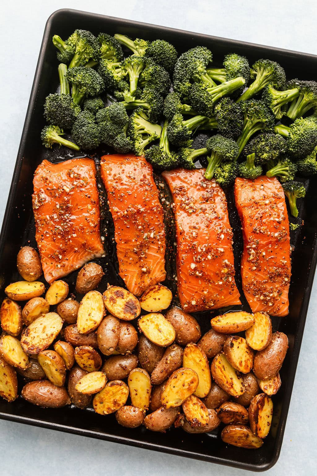 Overhead view of a sheet pan filled with salmon, potatoes, and broccoli ready for roasting