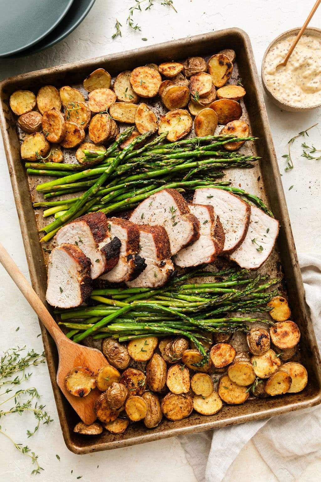Overhead view of a Sheet Pan Pork Tenderloin with roasted potatoes and asparagus topped with fresh herbs and seasonings. 