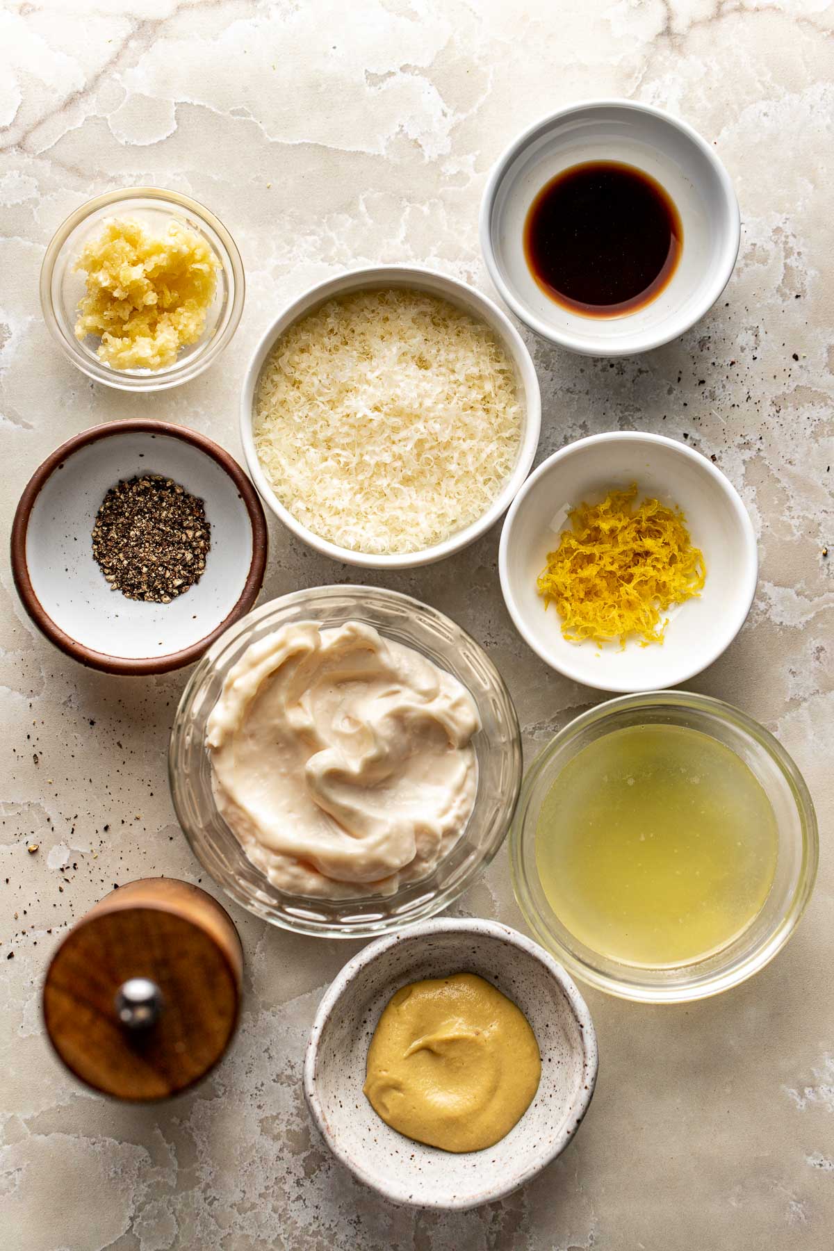 Overhead view of a variety of ingredients for Homemade Caesar Dressing in different sized bowls. 