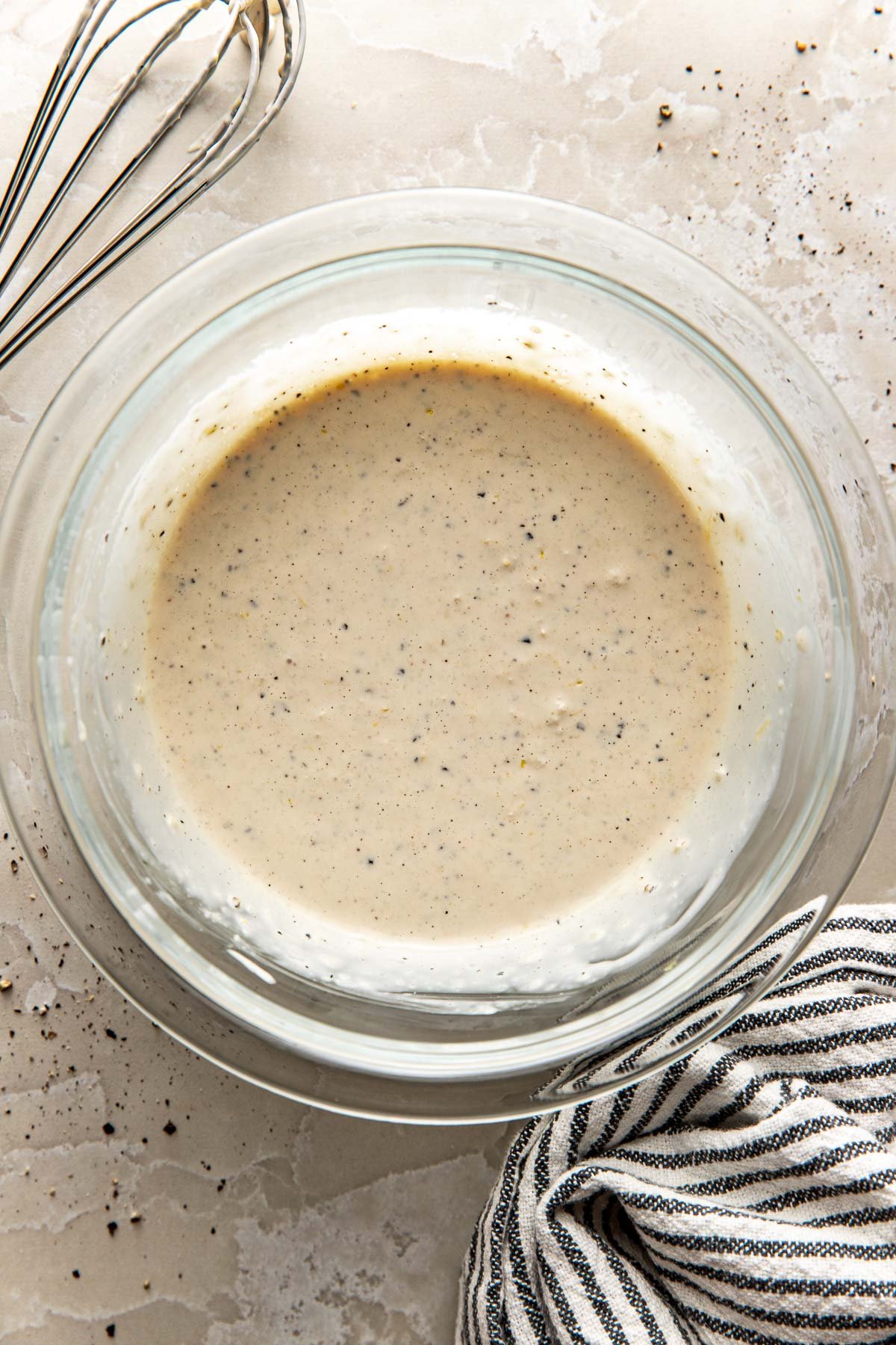 Overhead view of a glass bowl of Homemade Caesar Dressing with a whisk beside it. 