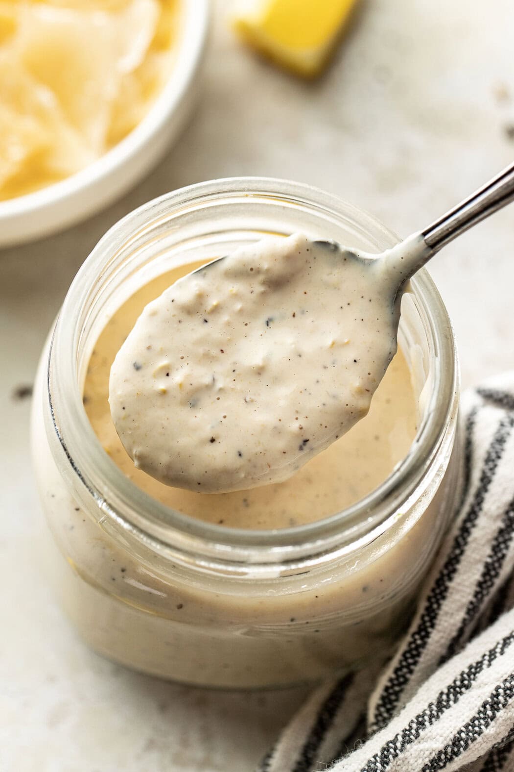 Close up view of a spoonful of Homemade Caesar Dressing coming out of a glass jar