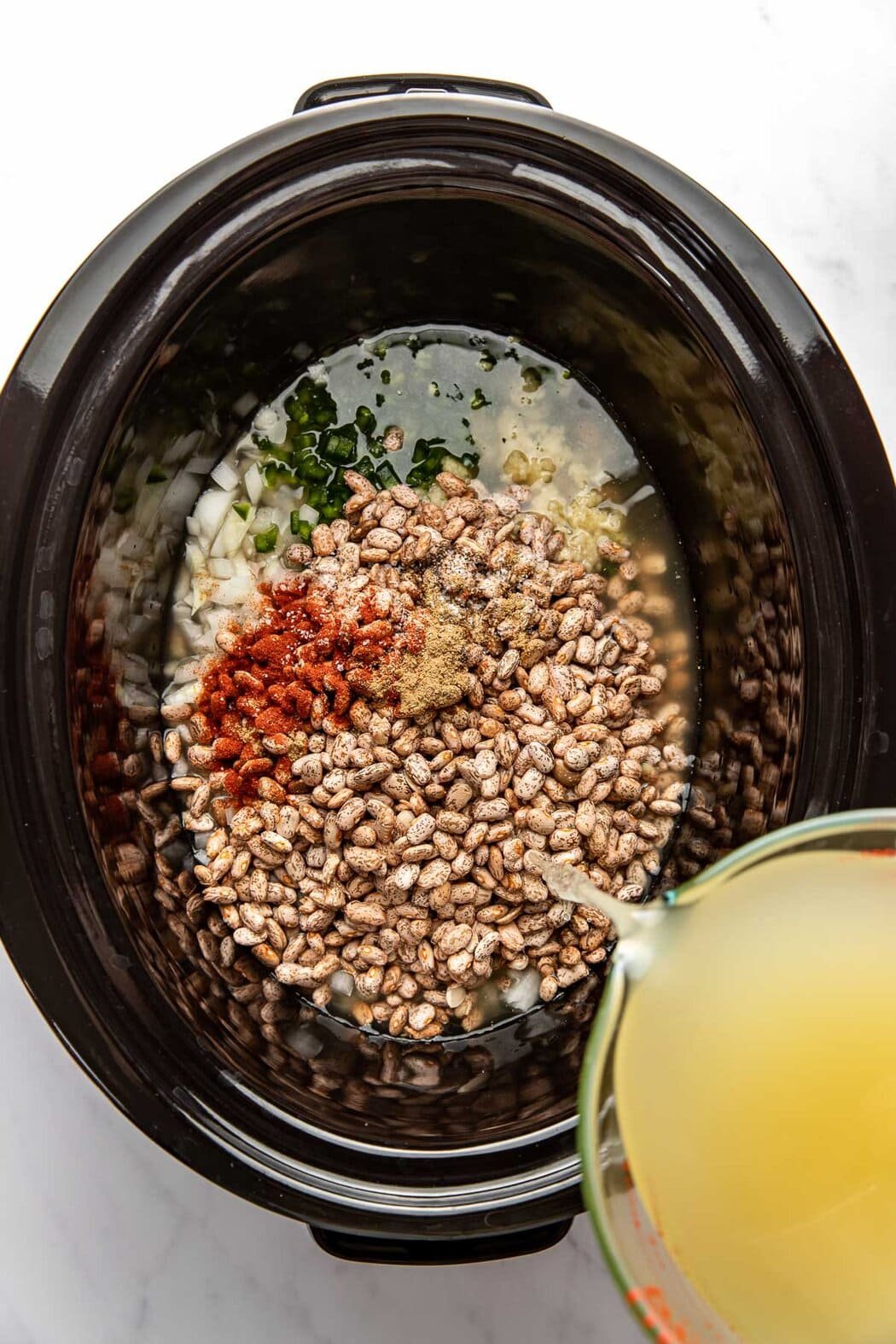 Overhead view of a slow cooker being filled with ingredients. 
