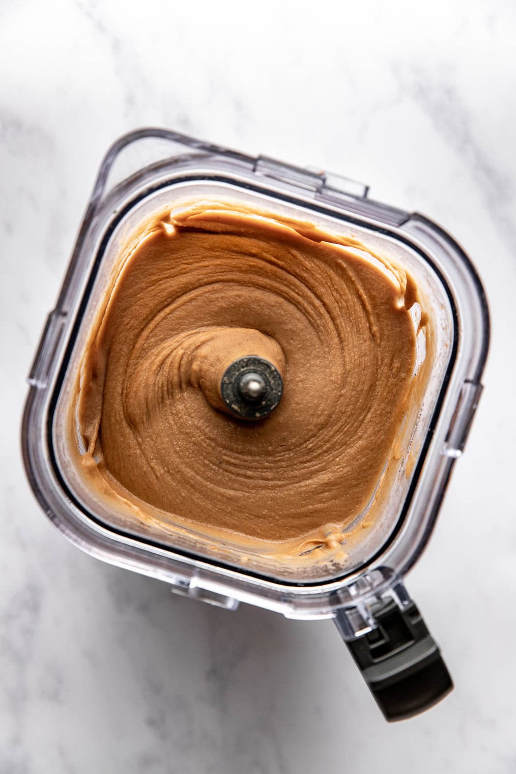 Overhead view of the inside of a blender filled with refried beans as a creamy consistency.