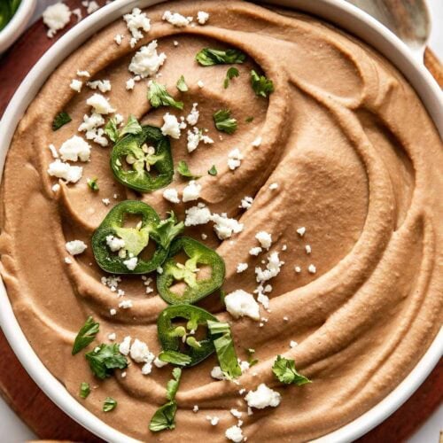 Overhead view of a bowl of creamy refried beans topped with cheese, jalapenos, and fresh cilantro.