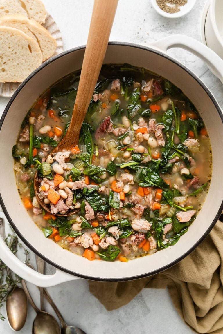 Overhead view of a Dutch oven filled with Ham and Bean soup and a wooden spoon in the pot.  
