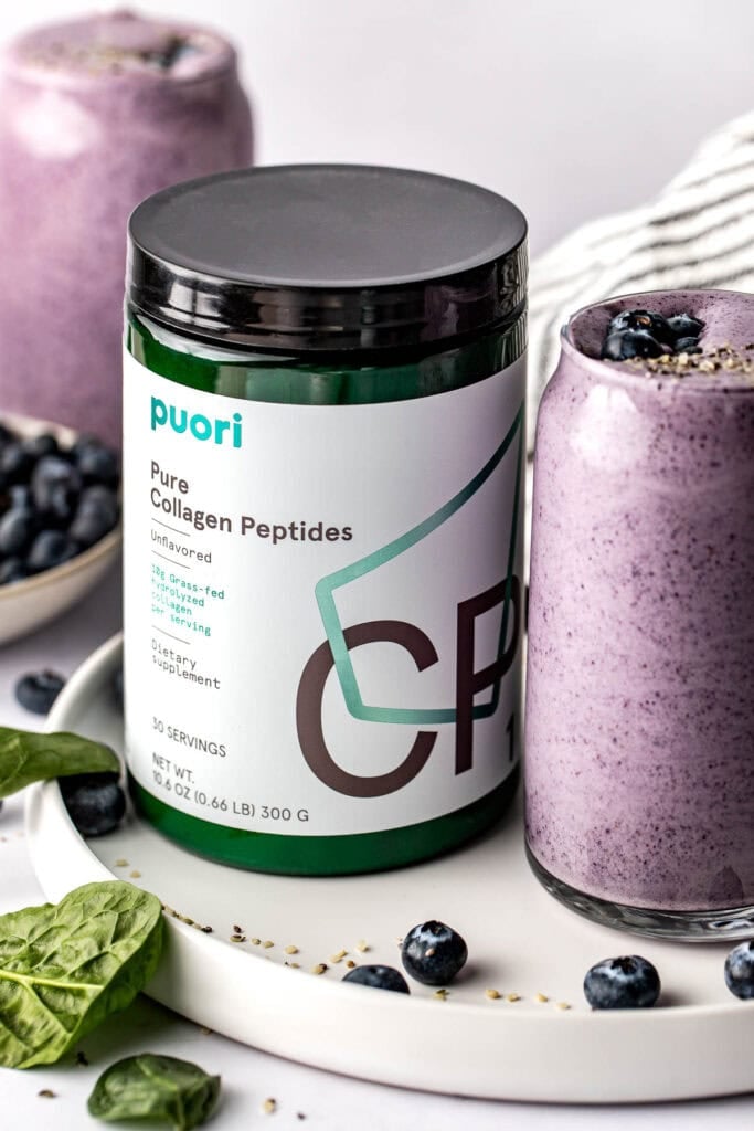 Close up view of a canister of collagen next to a deep purple smoothie