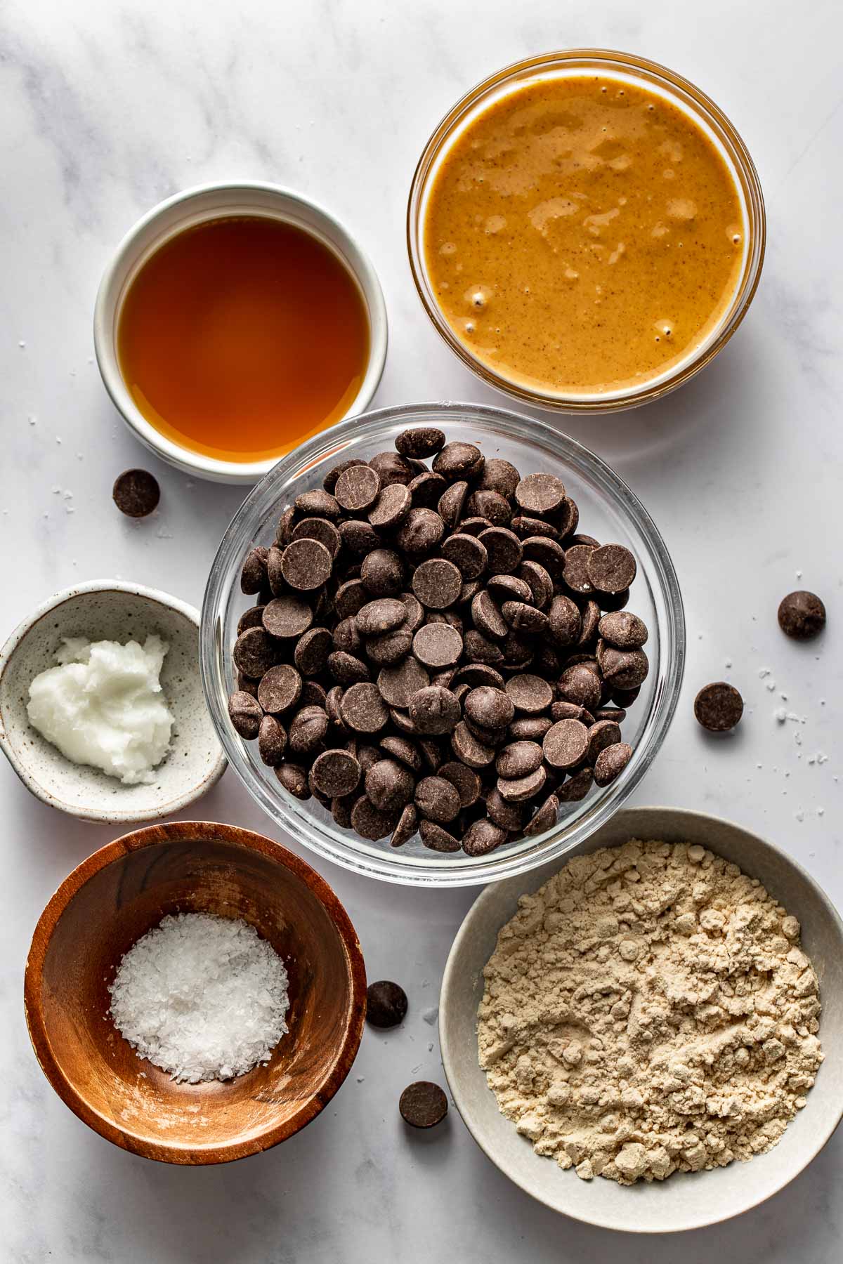 A variety of ingredients for Peanut Butter Protein Cups in different sized bowls on a white marble countertop