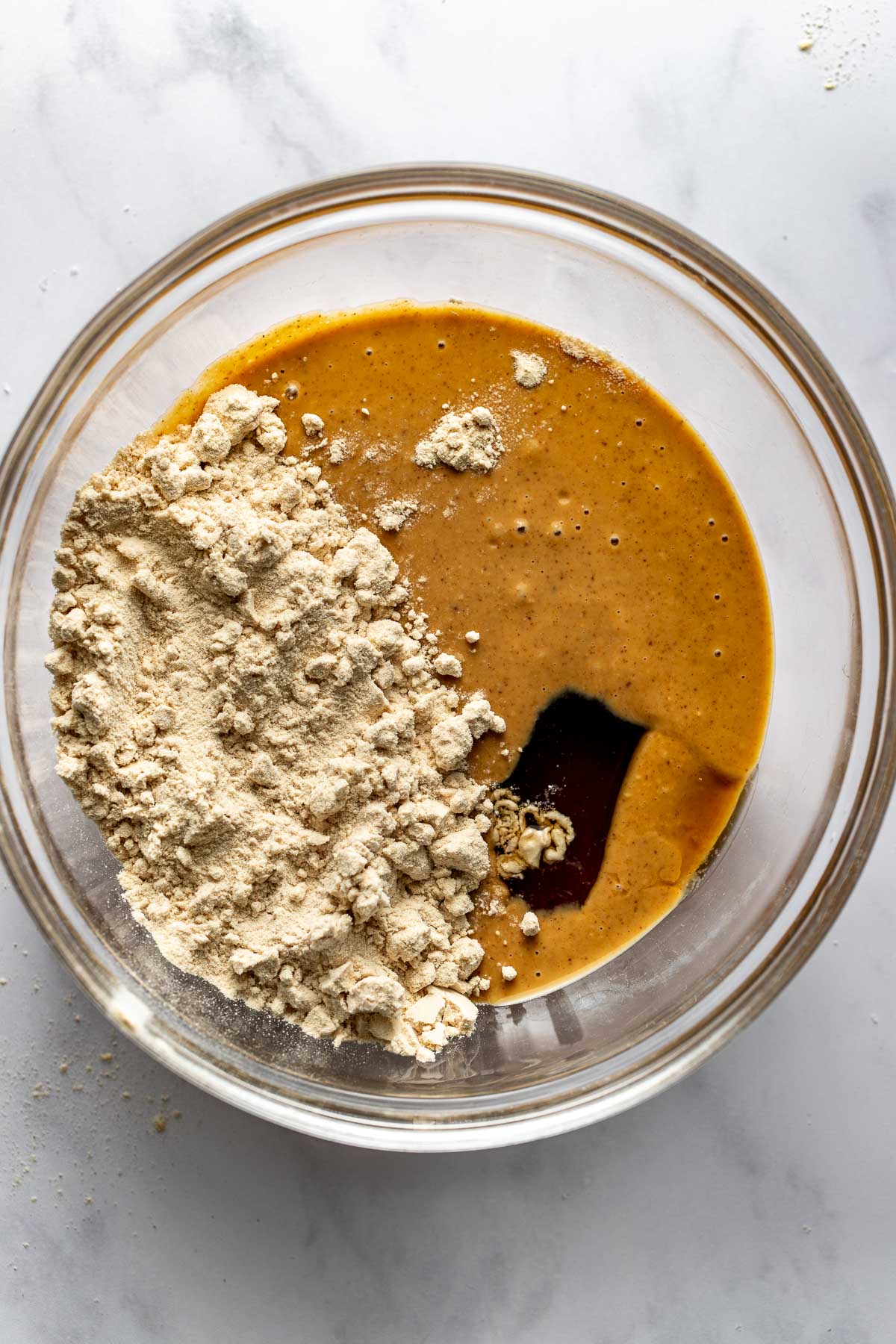 Overhead view of a glass bowl filled with peanut butter, protein powder, and maple syrup ready for mixing.