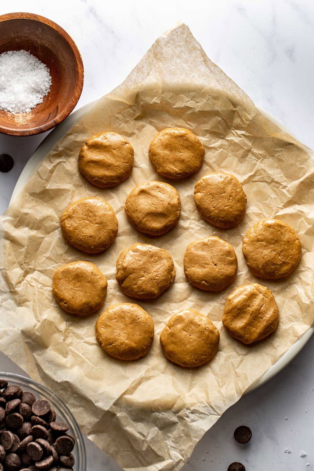 A plate covered with parchment paper topped with 12 peanut butter protein centers for Peanut Butter Protein Cups