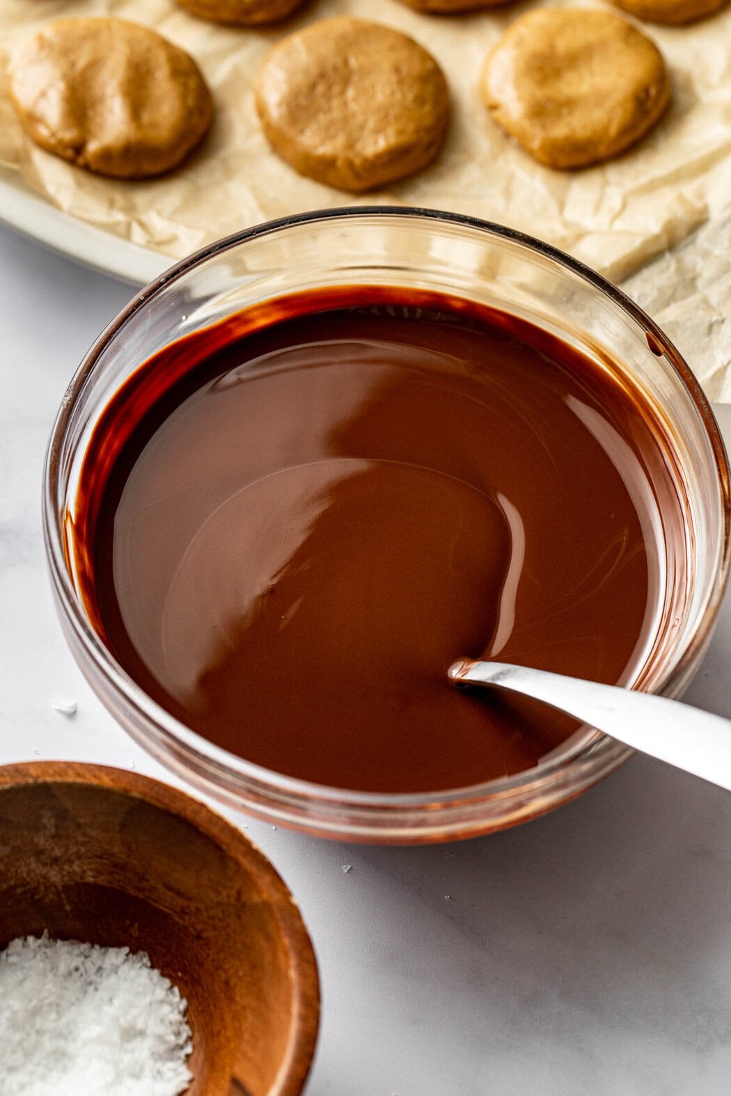 Overhead view of a glass bowl of melted chocolate with a silver spoon in the bowl