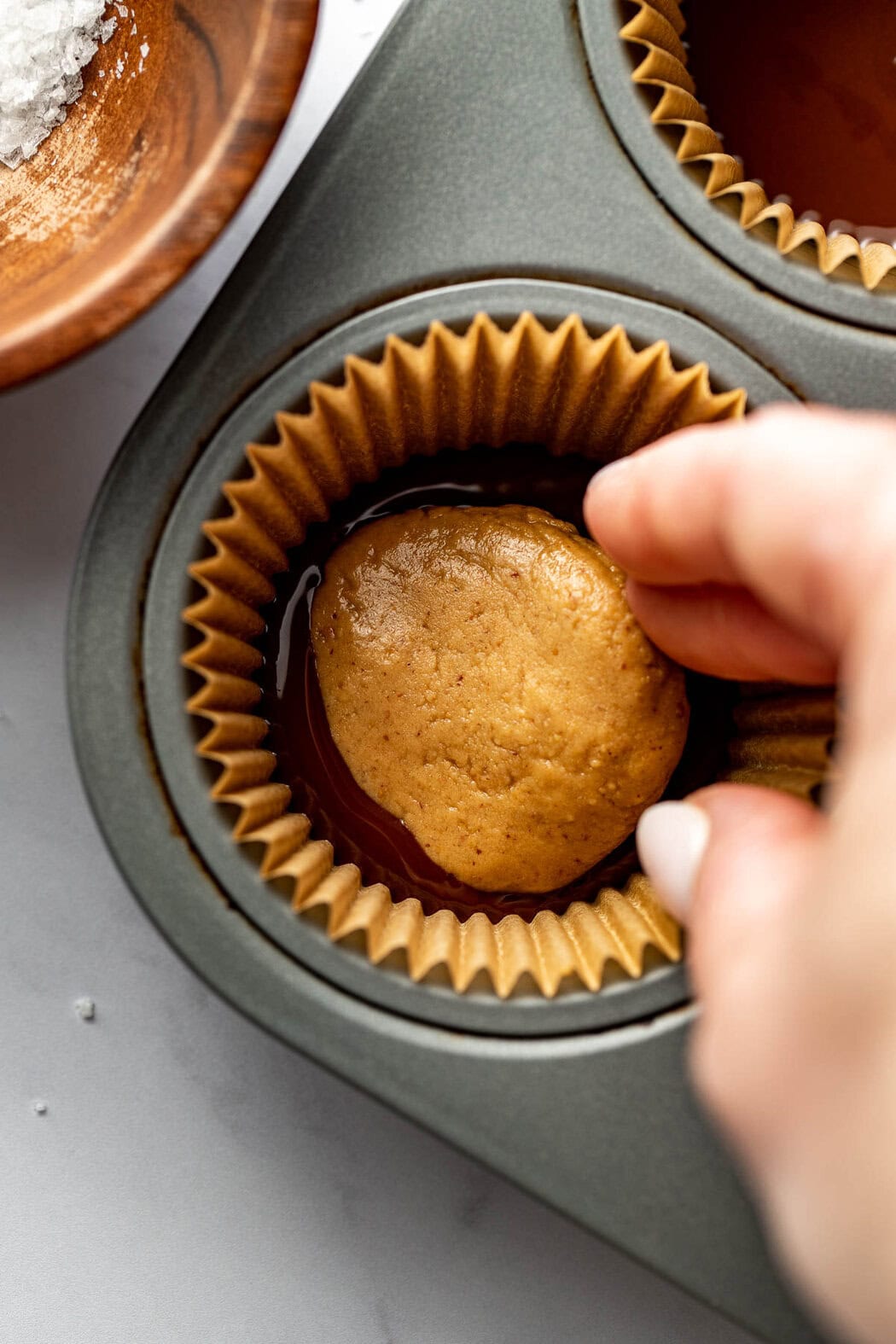 Overhead view of a hand placing a peanut butter protein disk on top of melted chocolate in a muffin tin well that is lined with a cupcake liner