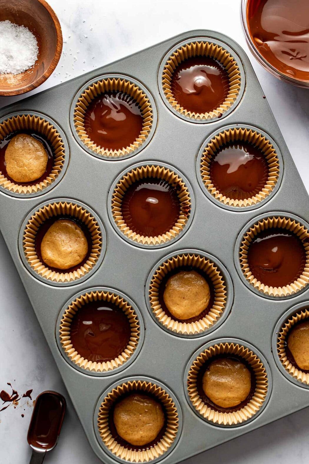 Overhead view of a muffin pan filled with Peanut Butter Protein Cups being topped with melted chocolate