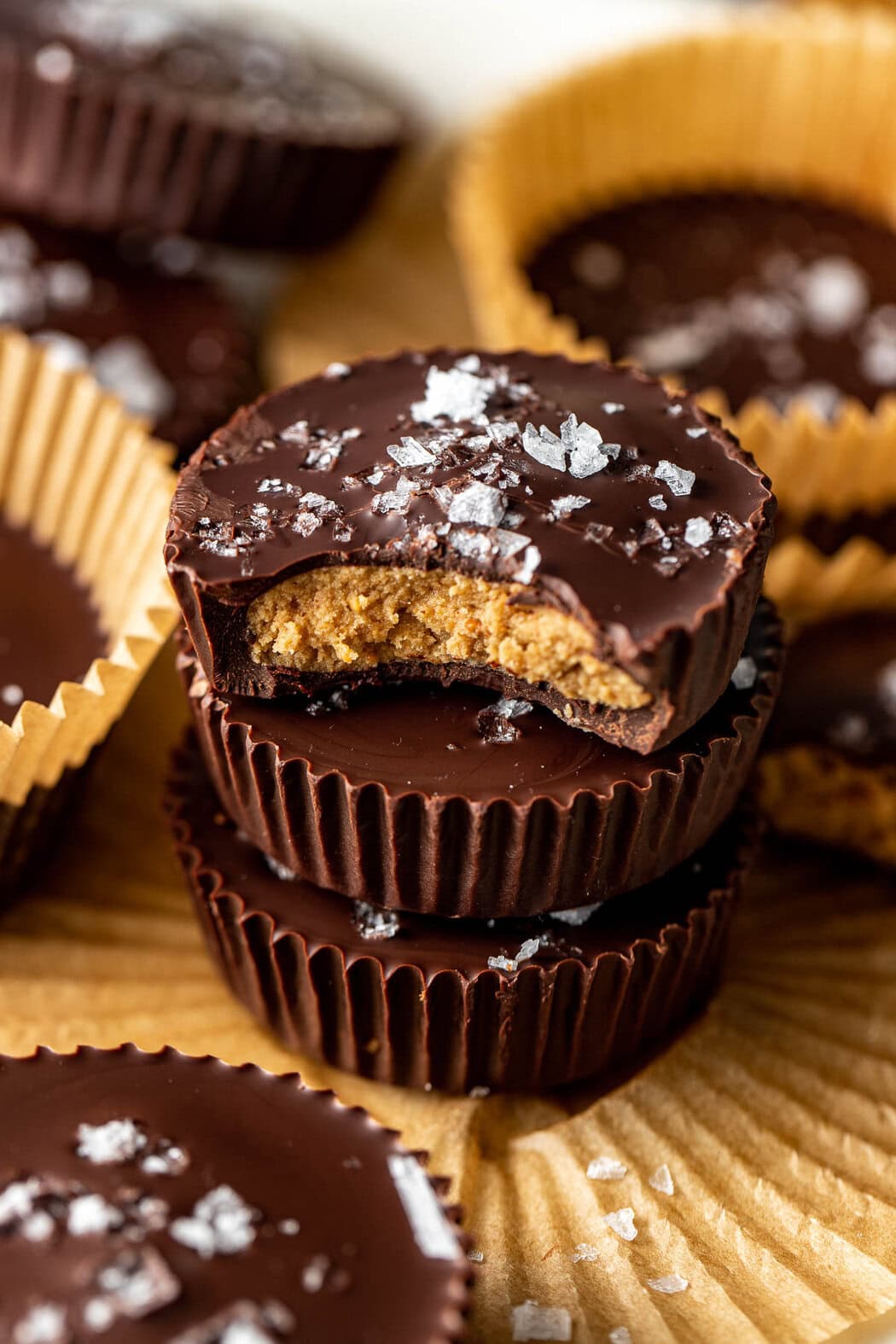 Close up view of a stack of Peanut Butter Protein Cups with the top one having a bite mark out of it showing the peanut butter middle, topped with flakey sea salt