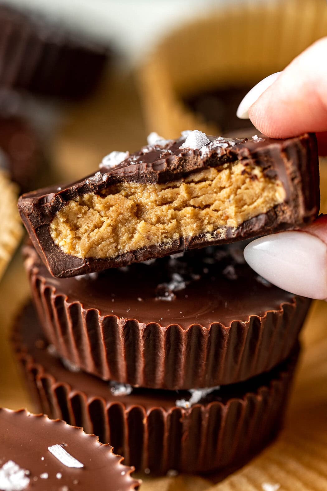 Close up view of a stack of Peanut Butter Protein Cups with a hand grabbing the top one that has a bite out of it showing the peanut butter center