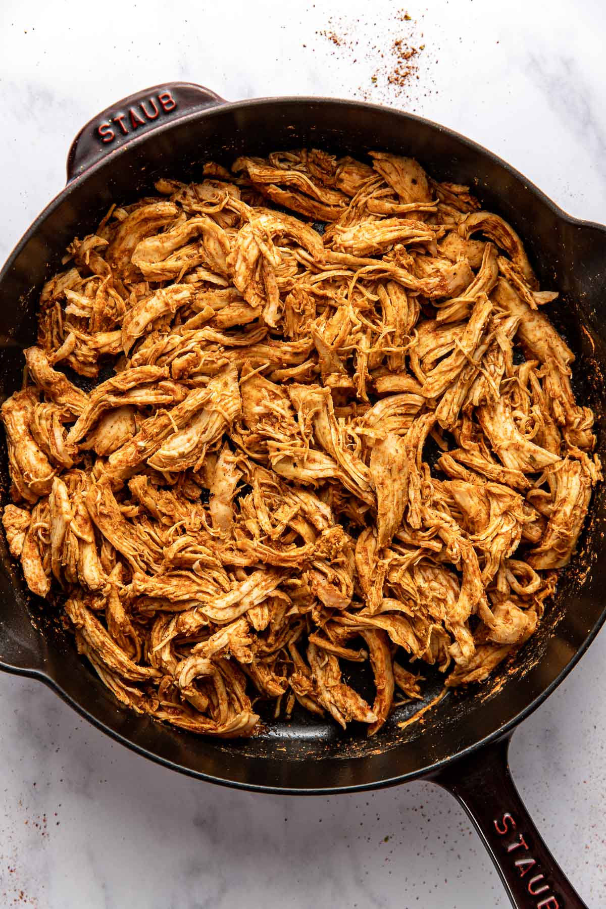 Overhead view of a skillet of shredded chicken seasoned with taco seasonings. 