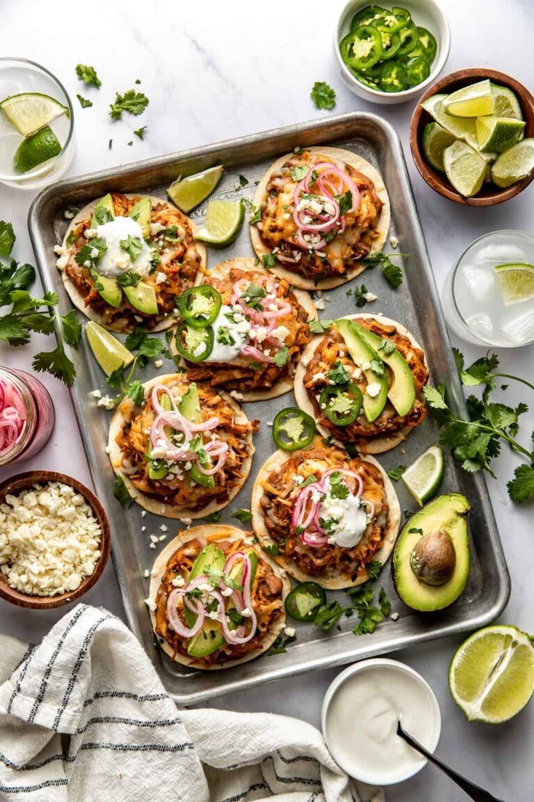 Overhead view of a sheet pan filled with chicken tostadas topped with avocado.