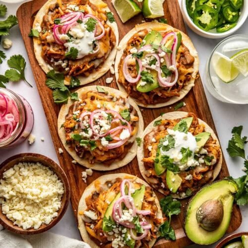 Overhead view of Sheet Pan Chicken Tostadas on a wooden cutting board topped with cilantro and sour cream.