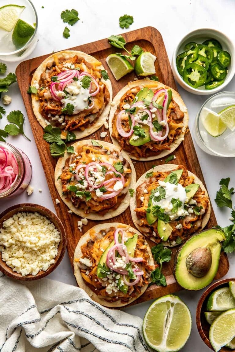 Overhead view of a wooden cutting board filled with chicken tostadas topped with pickled red onions.
