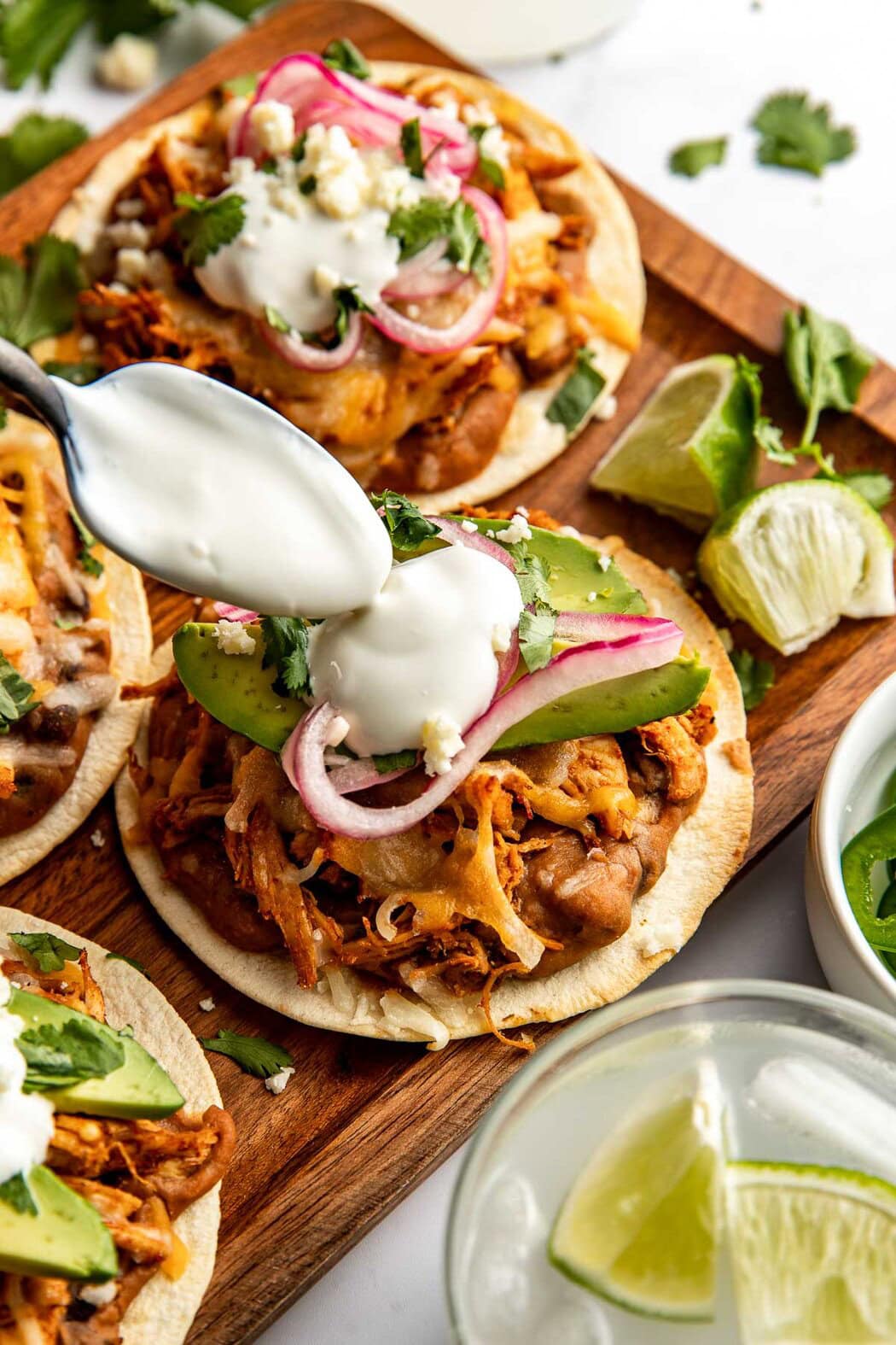 Close up view of a spoon placing a dollop of sour cream on a freshly baked chicken tostada. 