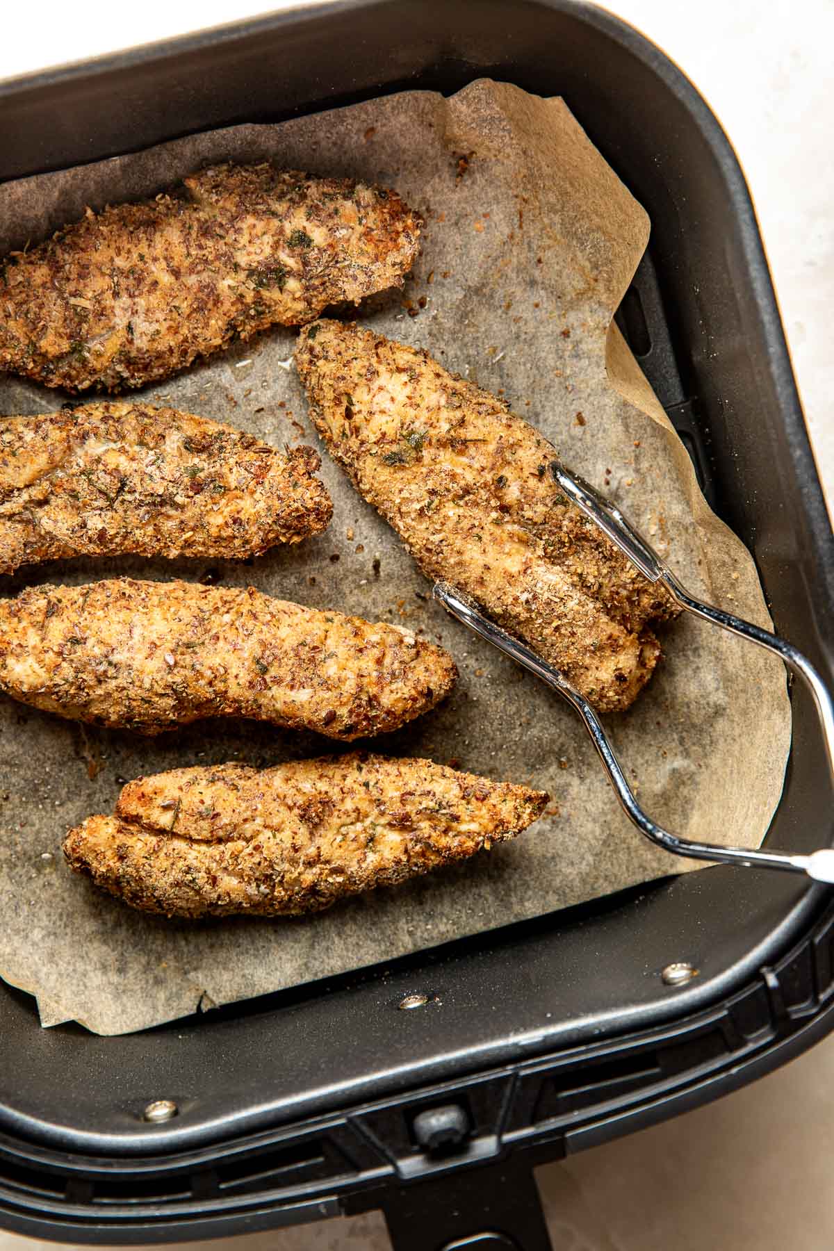 Close up view of freshly baked Air Fryer Chicken Tenders in an air fryer basket