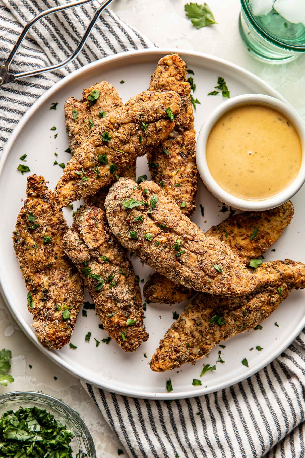 Overhead view of a plate of Air Fryer Chicken Tenders with a side of honey mustard topped with fresh green herbs and flakey sea salt.