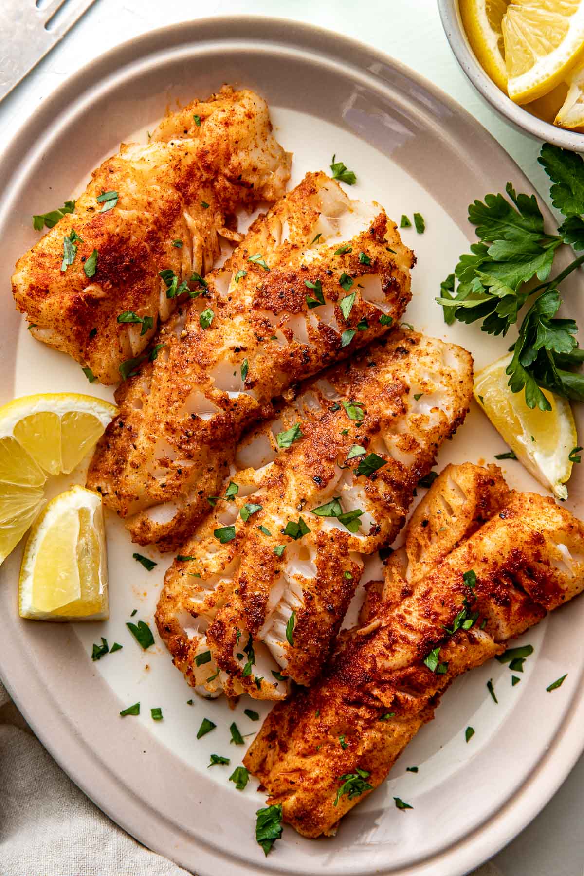 Overhead view of a plate of Air Fryer Cod strips topped with fresh herbs and lemon wedges. 