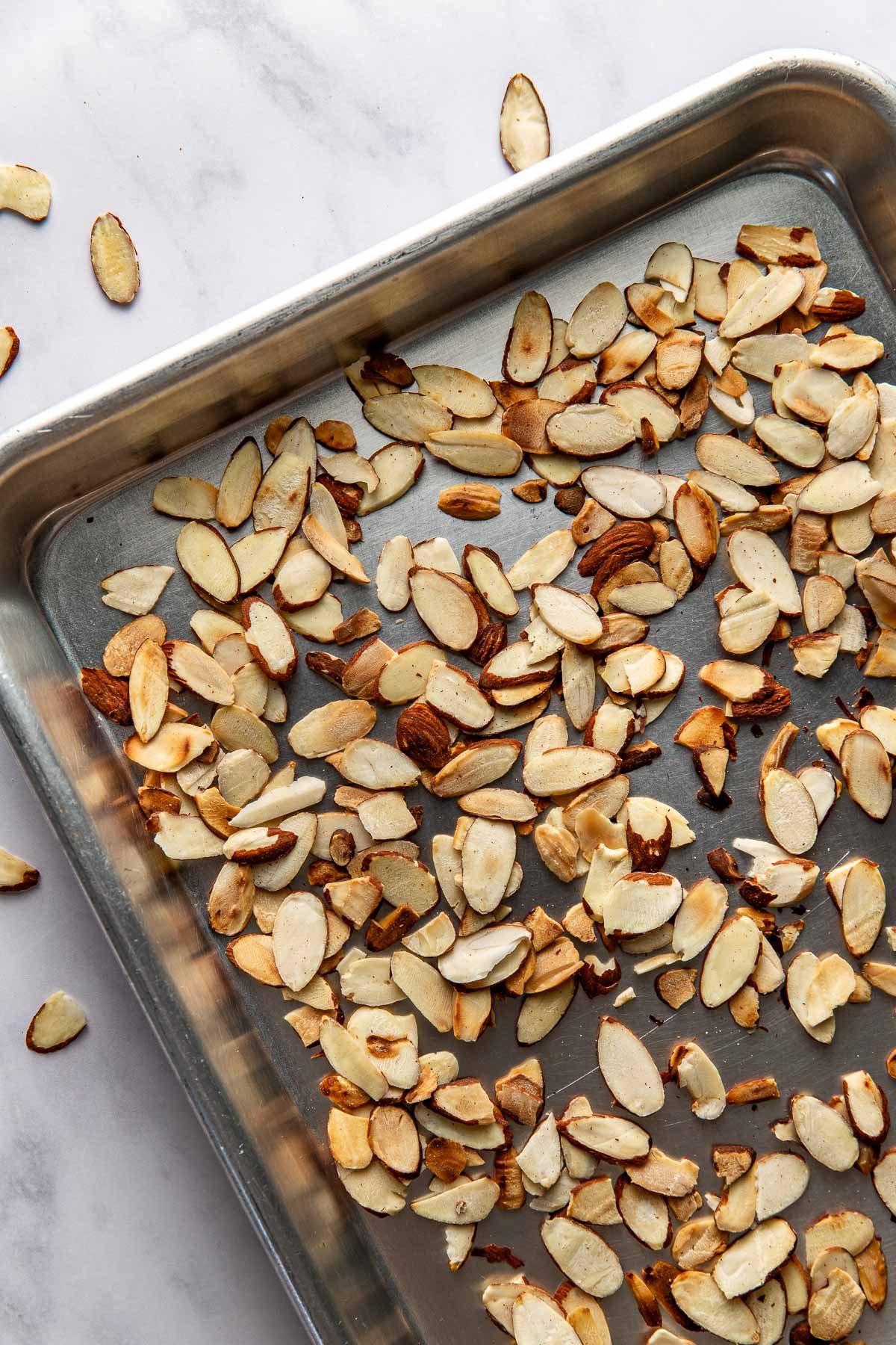 Overhead view of a sheet pan of sliced toasted almonds slightly browned in color. 
