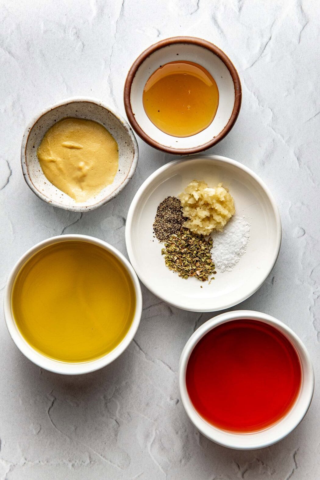 Overhead view of a variety of bowls filled with ingredients for Red Wine Vinaigrette in different sized bowls. 