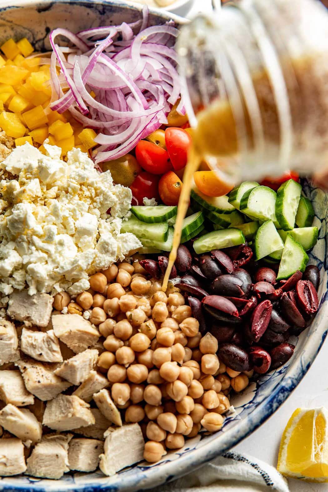 Close up view of a colorful Mediterranean salad with a hand pouring a jar of Red Wine Vinaigrette over the top.  