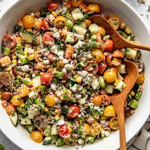 Overhead view of a bowl of summer salad topped with fresh herbs and crunchy sunflower seeds.