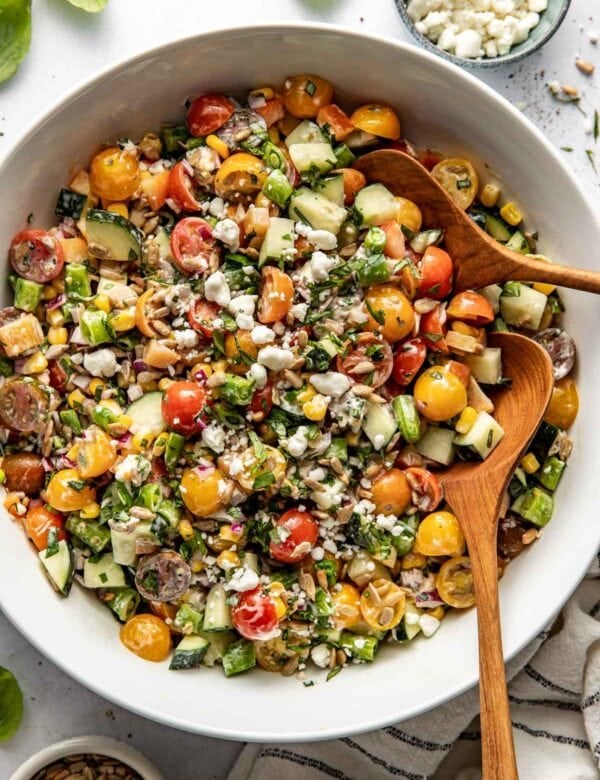 Overhead view of a bowl of summer salad topped with fresh herbs and crunchy sunflower seeds.