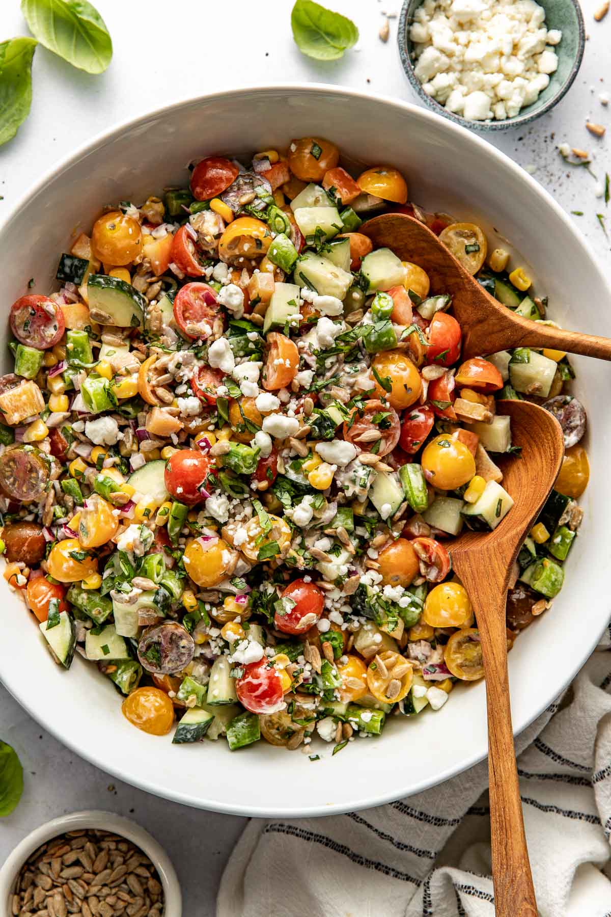 Overhead view of a large bowl of colorful summer salad topped with fresh herbs and crumbles of creamy goat cheese. 