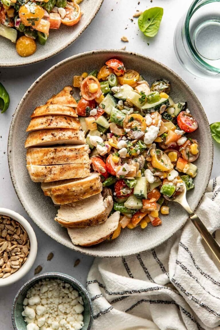 Overhead view of a plate of a sliced chicken breast with a colorful summer salad on the side topped with goat cheese crumbles. 