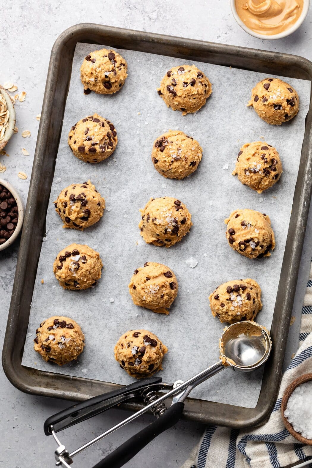 Overhead view of a sheet pan lined with parchment paper filled with balls of Chickpea Cookie Dough topped with flakey sea salt. 