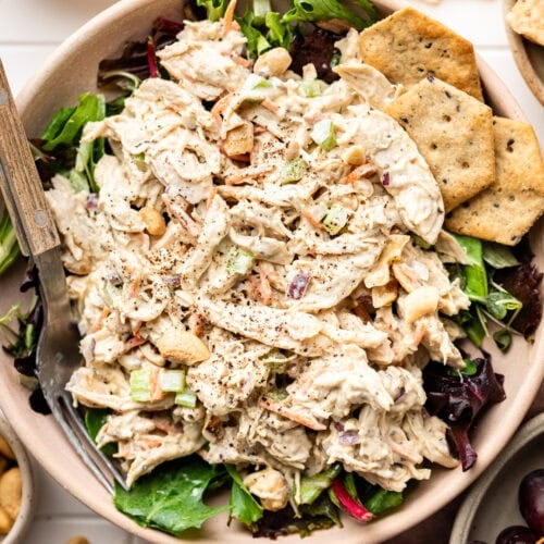 Overhead view of a bowl of Honey Mustard Chicken Salad on top of a bed of lettuce with multigrain crackers on the side.