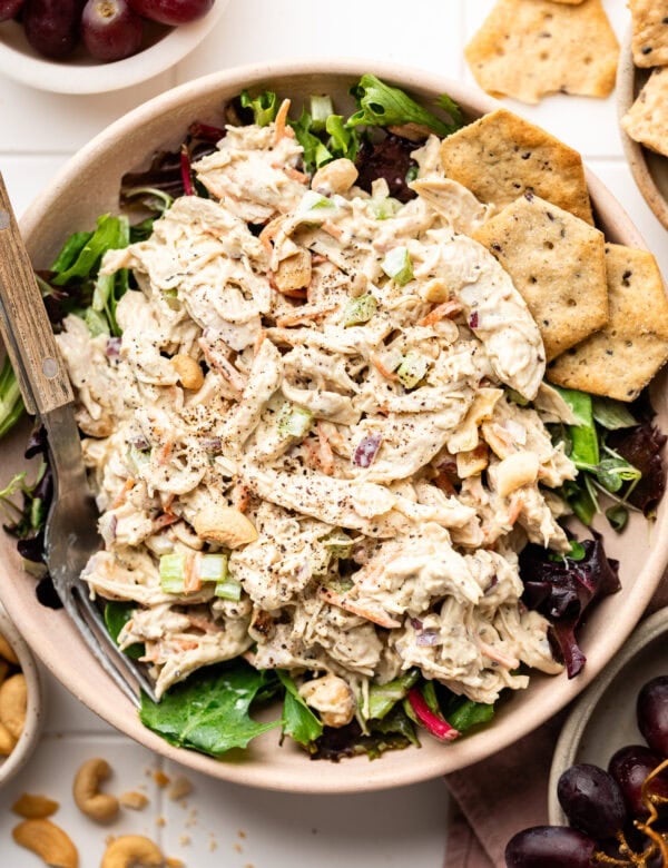 Overhead view of a bowl of Honey Mustard Chicken Salad on top of a bed of lettuce with multigrain crackers on the side.