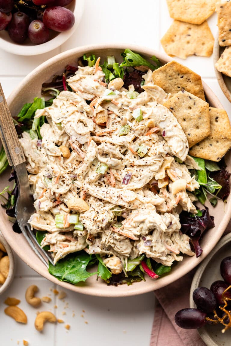 Honey mustard chicken salad served over a bed of greens in a bowl, crackers on the side. 