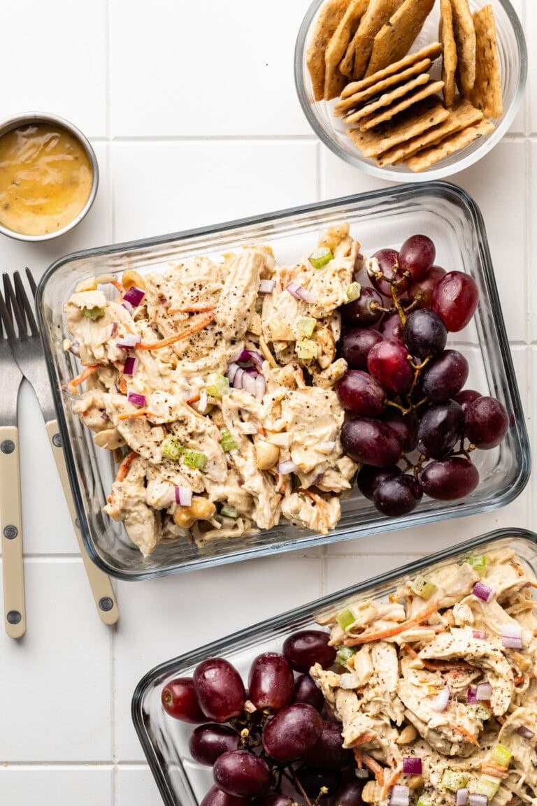 Overhead view of two glass meal prep containers filled with honey mustard chicken salad and a side of grapes.