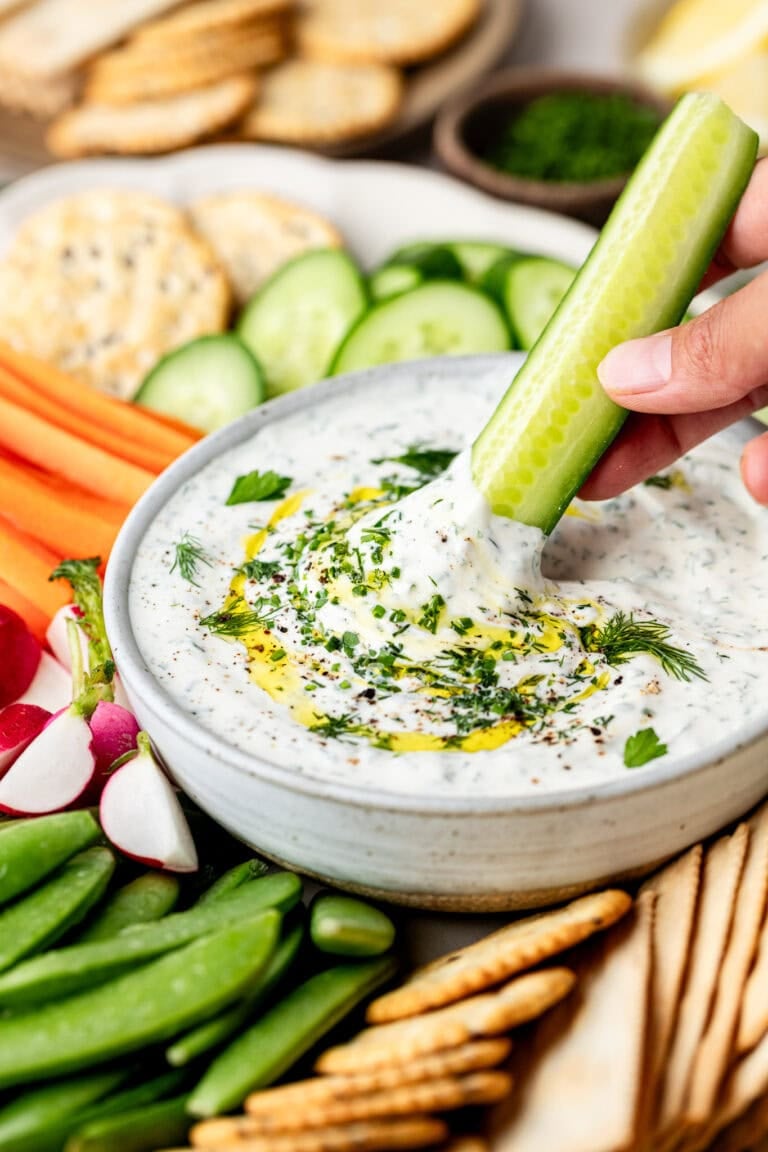 Close up view of a hand dipping a cucumber in a whipped cottage cheese dip.