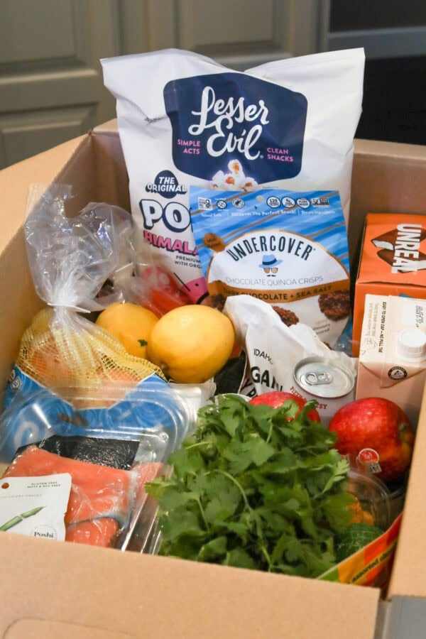 Photo of cardboard box on a countertop filled with a variety of fresh produce and packaged foods.
